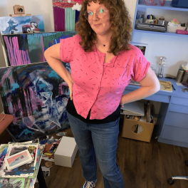 Nicolette Yates wearing a pink shirt and standing in her art studio.